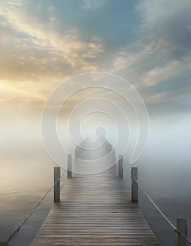 Pier going into the foggy sea or lake with moody sky at sunset