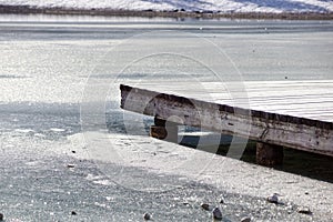 Pier on the lake. Wooden bridge in forest in winter time with blue frozen lake. Lake for fishing with pier. Dark lake