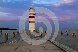 A pier leading to the lake and a red and white lighthouse on Lake Neusiedl in Podersdorf, Austria. In the background is a dramatic