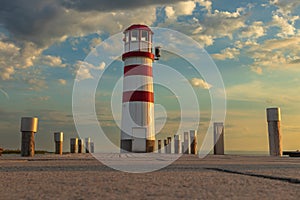 A pier leading to the lake and a red and white lighthouse on Lake Neusiedl in Podersdorf, Austria. In the background is a dramatic