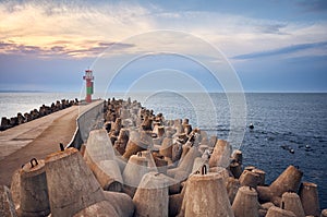 Pier with lighthouse protected by concrete breakwater tetrapods at sunset