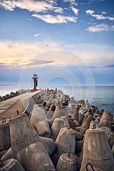 Pier with lighthouse protected by concrete breakwater tetrapods at sunset