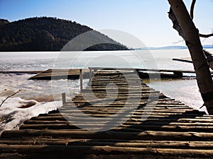 Pier from the logs on the frozen lake in the mountain forest