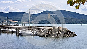 A pier made of concrete and boulders with boats moored in Lake Trasimeno Umbria, Italy