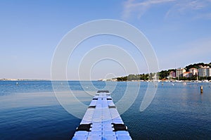 The pier near beach against blue sky in sunny day. Adriatic coast and sea in Slovenia. Holiday and travel concept