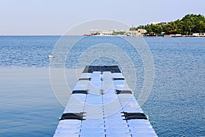The pier near beach against blue sky in sunny day. Adriatic coast and sea in Slovenia. Holiday and travel concept