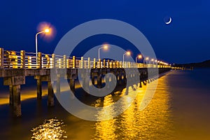 Pier at night with yellow lights on a background of blue sky