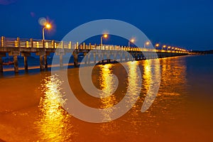 Pier at night with yellow lights on a background of blue sky