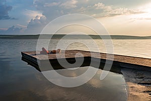 Pier with ottomans at calm lake at sunset