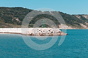 The pier of Pesaro harbor with breakwater tetrapods and a small green lighthouse Italy, Europe