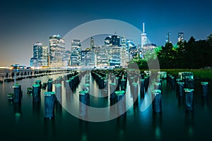 Pier pilings and the Manhattan skyline at night, seen from Brook