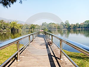 The pier in public park with danger warning sign. Silver handrail with wooden walkway near the lake with landscape view