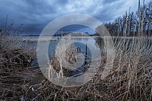 A pier in the reeds and a dark cloud over the lake