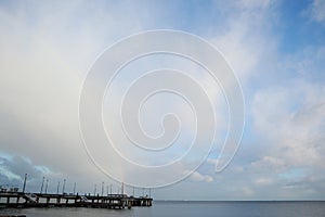 Pier on the sea beach. Cloudy sky with rainbow. Rainbow on the sea in cloudy weather.