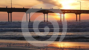 Pier in sea water on beach. Ocean waves, sky at sunset. California coast vibes.