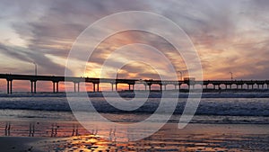 Pier in sea water on beach. Ocean waves, sky at sunset. California coast vibes.