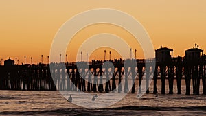 Pier silhouette at sunset, California USA, Oceanside. Surfing resort, ocean tropical beach. Surfer waiting for wave.