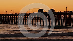 Pier silhouette at sunset, California USA, Oceanside. Surfing resort, ocean tropical beach. Surfer waiting for wave.