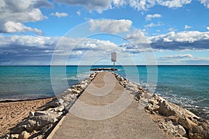 A pier of stones, a pier going into the sea. Dramatic sky with dark, heavy clouds