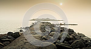 Pier surrounded by stones going through the calm sea with the sunny sky in the background