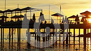 pier with umbrellas and sunbeds. silhouettes. beautiful sunset on sea.