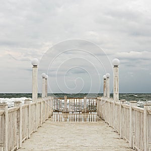 Pier with white wooden handrails at sea during a storm.