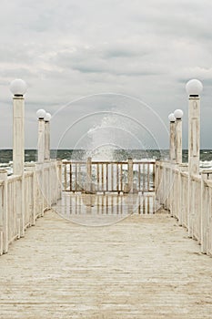 Pier with white wooden handrails at sea during a storm.