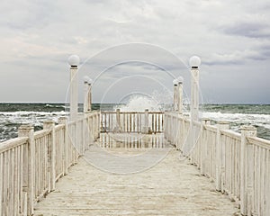 Pier with white wooden handrails at sea during a storm.