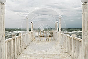 Pier with white wooden handrails at sea during a storm.