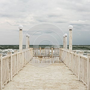 Pier with white wooden handrails at sea during a storm.