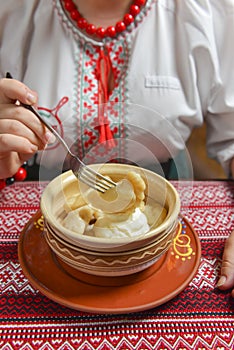 Pierogi or pyrohy, varenyky, traditional dumplings served with sour cream in bowl on wooden table.