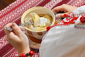 Pierogi or pyrohy, varenyky, traditional dumplings served with sour cream in bowl on wooden table.