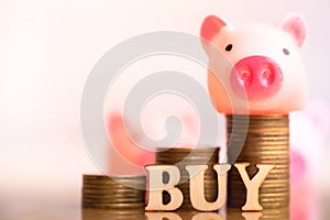 Pig on coins stack and wood block word BUY.