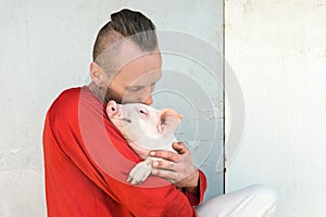 Pig farmer with cute piglet in hands at farm wall. Focus on piggy