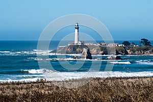 Pigeon Point Lighthouse, landscape view with brush and ocean waves in the foreground, on a clear sunny day on the California Coast