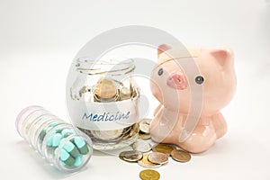 A piggy bank with a bandage at head with a pill container and an glasss bottle filled with coins on white background