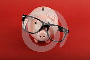 Piggy bank with black falling glasses on red background