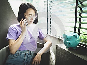 Piggy bank with blurry background of woman using smart phone, booking hotel online, saving money for vacation concept, lifestyle