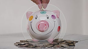 Piggy bank business standing on a pile of coins concept. A hand is putting a coin in a lifestyle piggy bank on a yellow