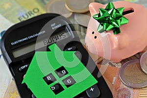 Piggy bank with calculator and paper house on euro money background - Concept of saving money to buy a home and money bonus