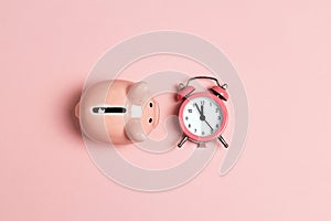 Piggy bank and classic alarm clock on pink background. Time to saving, money, banking concept.