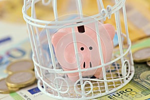 Piggy bank closed in a cage on euro money - Concept of savings blocked