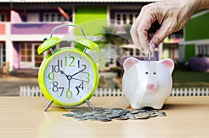 Piggy bank with coin and alarm clock on wood table background