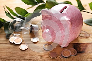 Piggy bank with coins and light bulb on wooden background. Concept of saving energy