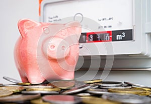 Piggy bank with coins near the natural gas meter at home. Energy saving or cost of natural gas for heating a house concept image.