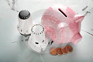 Piggy bank with coins and thermostats on light background. Heating saving concept