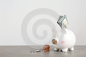 Piggy bank with dollar banknotes and house keys on table against white background