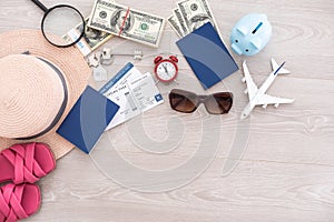 A piggy bank with dollar bills in a travel setting. In the composition of the image: Sun Hat, Alarm Clock. Concept of