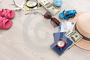 A piggy bank with dollar bills in a travel setting. In the composition of the image: Sun Hat, Alarm Clock. Concept of