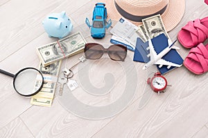 A piggy bank with dollar bills in a travel setting. In the composition of the image: Sun Hat, Alarm Clock. Concept of
